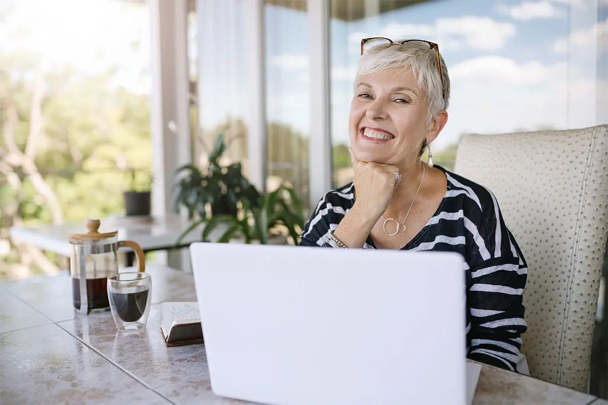 Senior woman at laptop computer in backyard while sitting in patio furniture